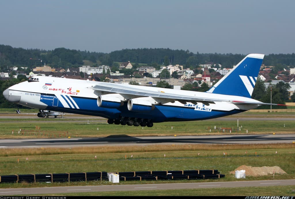 An-124 departing with hills and town in background